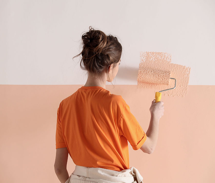 Painting Services - Woman painting a wall with a roller brush, focused and determined, adding a fresh coat of paint to the room.